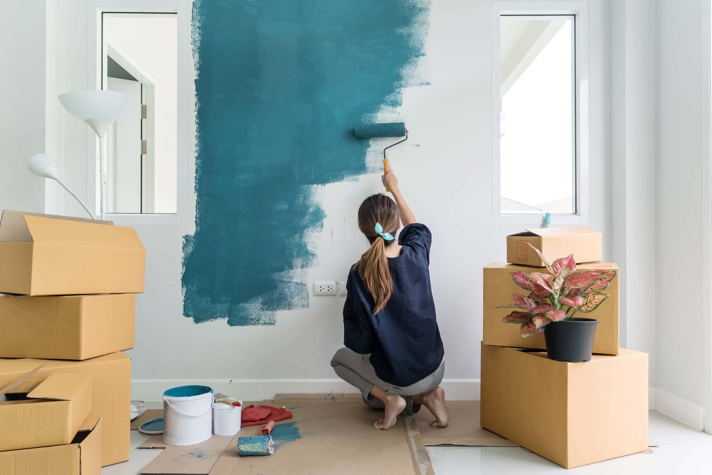 Mujer de espaldas, pinta un pared en color azul.