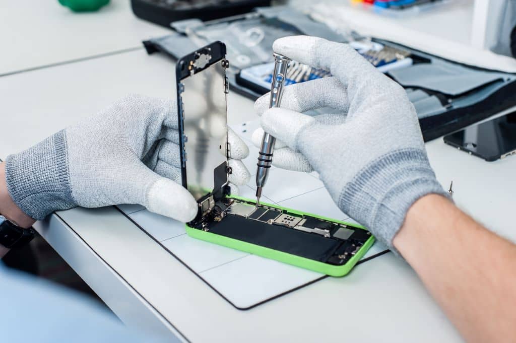 Técnico reparando un dispositivo móvil con herramientas avanzadas.