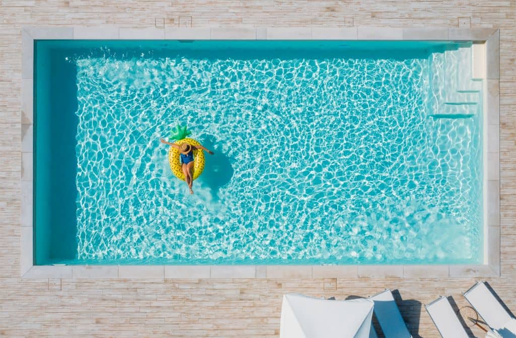 Piscina de obra en un jardín rodeado de vegetación y mobiliario de exterior. 