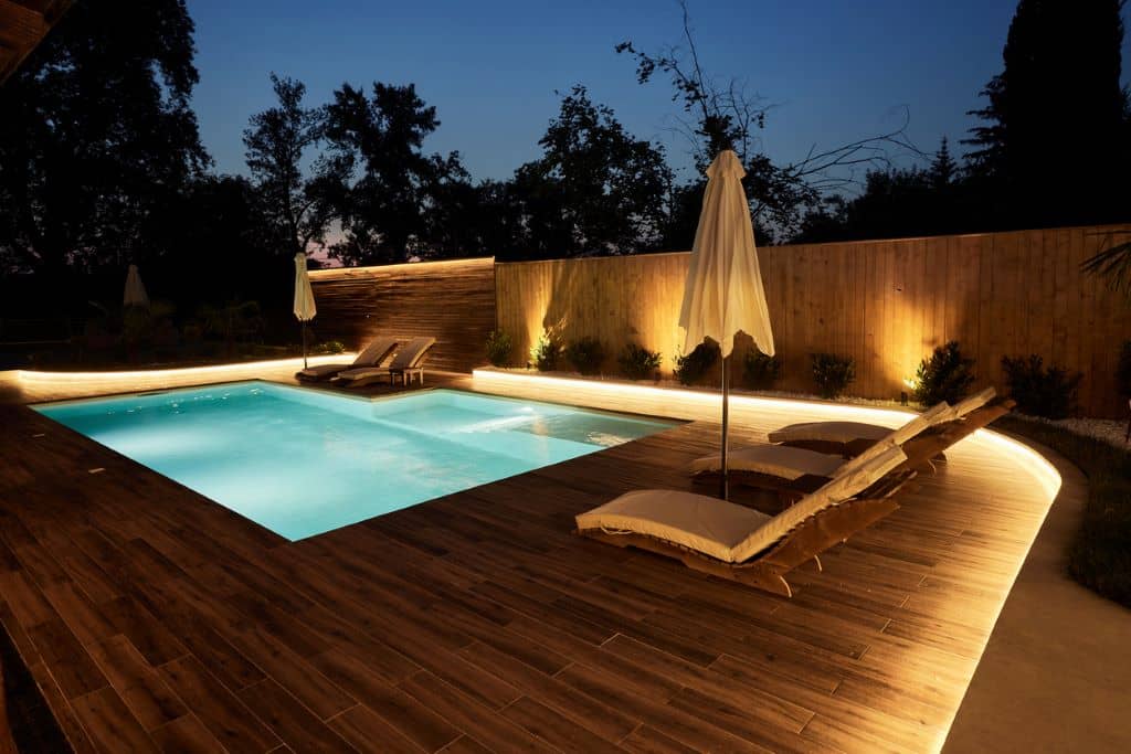 Piscina decorada con iluminación LED, muebles modernos y vegetación tropical, ideal para un espacio exterior acogedor. 