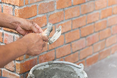 Manos preparando mezcla para reajuntar ladrillos de una pared